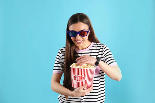 Junge Frau mit 3D-Gläsern und leckerem Popcorn auf farbigem Hintergrund — Stockfoto