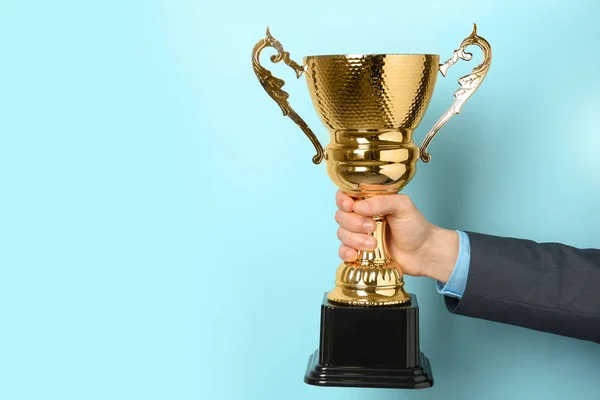 Hombre sosteniendo copa de trofeo dorado sobre fondo de color, primer plano. Espacio para texto — Foto de Stock