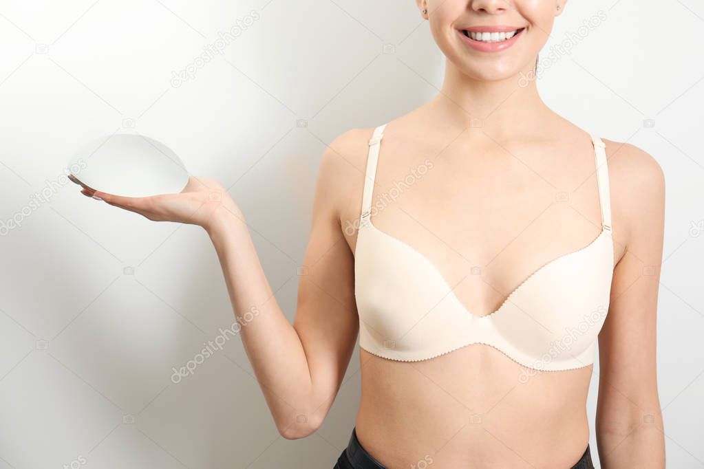 Woman holding silicone implant for breast augmentation on white background, closeup. Cosmetic surgery