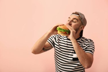 Genç adam renk arka plan üzerinde lezzetli hamburger yeme. Metin için yer
