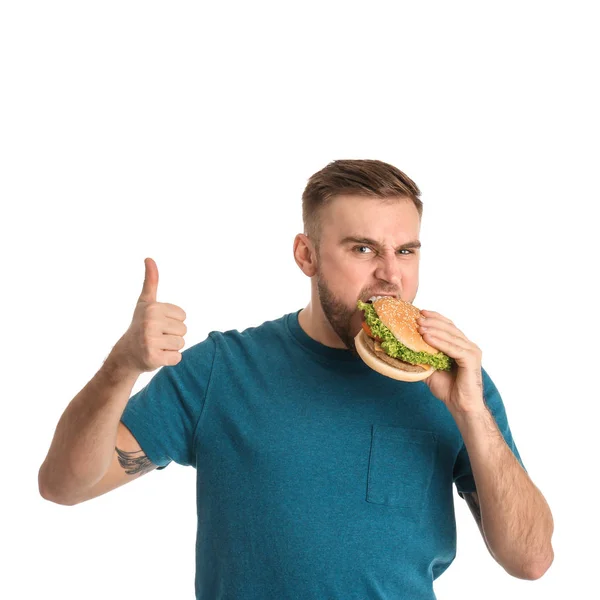 Jovem comendo hambúrguer saboroso no fundo branco — Fotografia de Stock