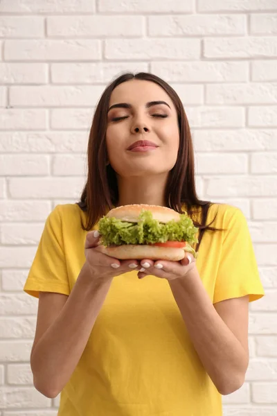 벽돌 벽 근처 맛 있는 햄버거를 먹고 젊은 여자 — 스톡 사진