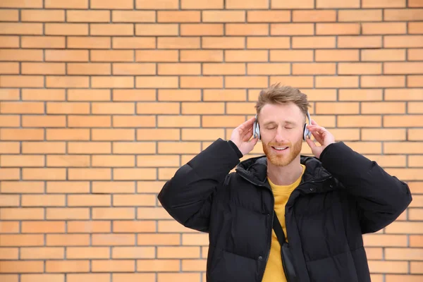 Young man listening to music with headphones against brick wall. Space for text — Stock Photo, Image