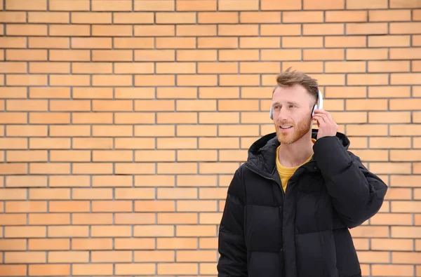 Ung man lyssnar på musik med hörlurar mot tegelvägg. Utrymme för text — Stockfoto