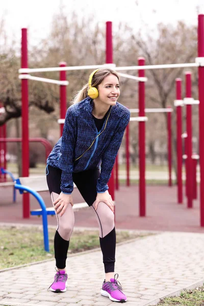 Young woman with headphones listening to music and exercising on sports ground