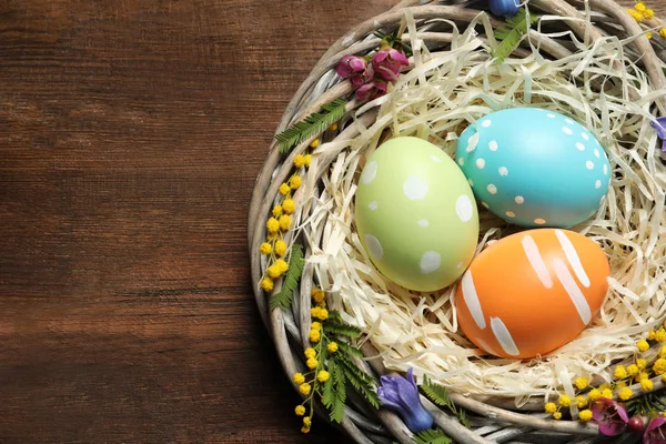 Nido de mimbre con huevos de Pascua pintados y flores en mesa de madera, vista superior. Espacio para texto —  Fotos de Stock