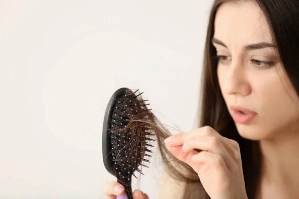 Mujer desenredando su cabello de cepillo sobre fondo claro. Espacio para texto — Foto de Stock