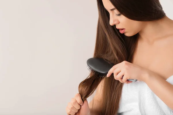 Woman struggles to brush her hair on light background. Space for text — Stock Photo, Image