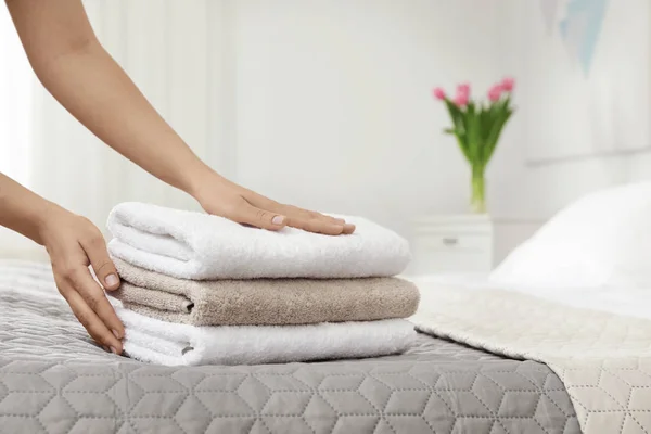 Νεαρή καθαρίστρια βάζοντας στοίβα πετσέτες στο κρεβάτι σε δωμάτιο ξενοδοχείου, κοντινό πλάνο — Φωτογραφία Αρχείου
