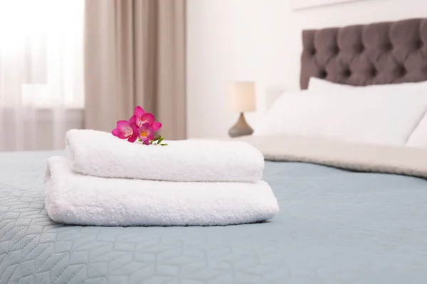 Stack of fresh towels with flowers on bed in hotel room — Stock Photo, Image