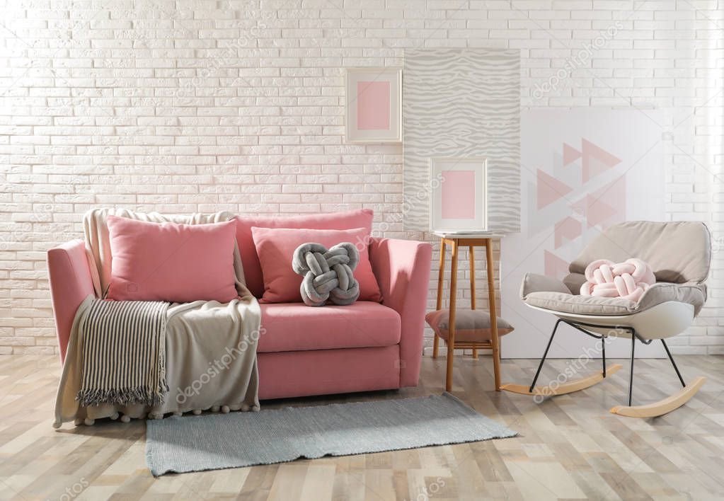 Stylish living room interior with sofa and rocking armchair near brick wall