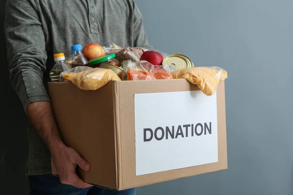 Man holding donation box with food on gray background, closeup — Stock Photo, Image