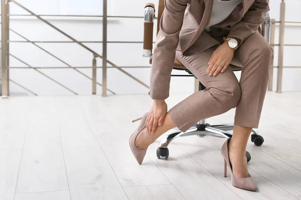 Giovane donna che soffre di dolore alle gambe in ufficio, primo piano con spazio per il testo — Foto Stock