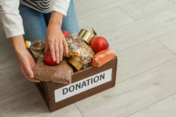 Mujer tomando comida de la caja de donación en el suelo de madera, primer plano con espacio para el texto —  Fotos de Stock