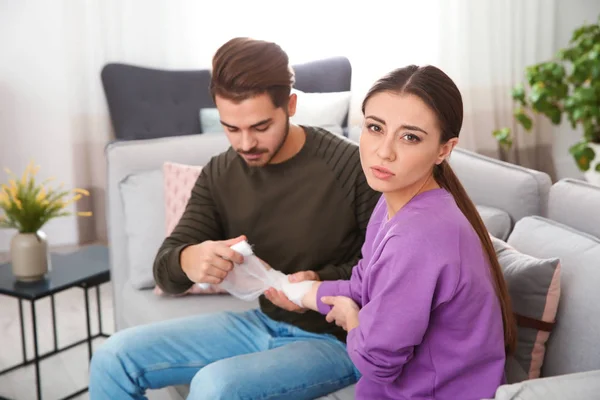 Νεαρός εφαρμόζοντας επίδεσμο για τραυματίες χέρι της γυναίκας στο σπίτι. Πρώτες βοήθειες — Φωτογραφία Αρχείου