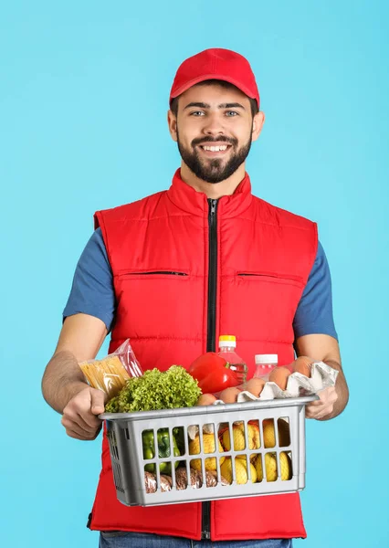 Человек держит корзину со свежими продуктами на цветном фоне. Доставка продуктов питания — стоковое фото