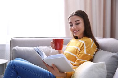 Evde kanepede kitap okumak kahve fincan genç kadınla