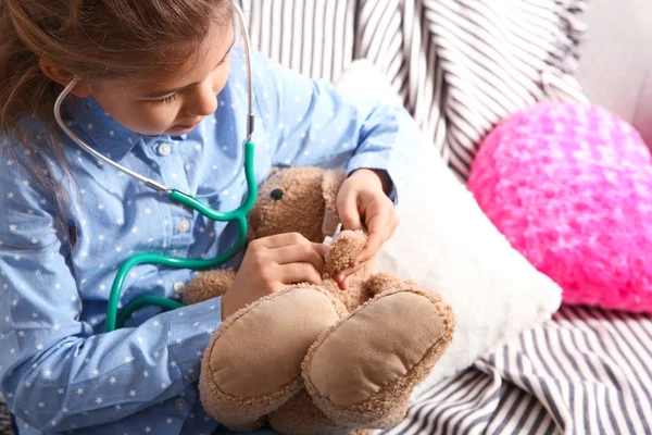 Söta barn inbillar sig själv läkare medan du spelar med stetoskop på soffan i vardagsrummet — Stockfoto