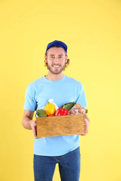 Leverans man håller trälåda med livsmedelsprodukter på färg bakgrunden — Stockfoto