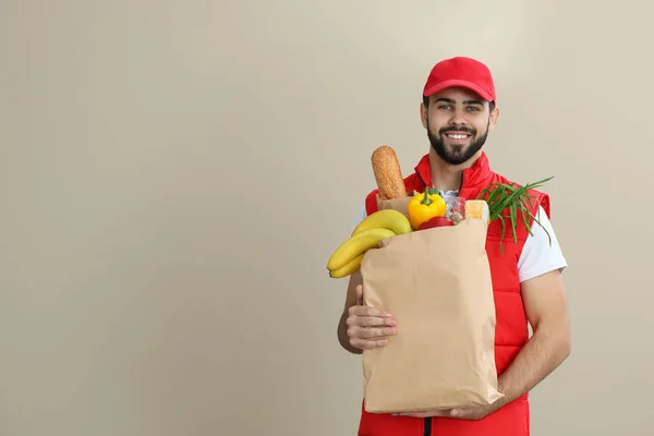 Мужчина держит бумажный пакет со свежими продуктами на цветном фоне, место для текста. Доставка продуктов питания — стоковое фото