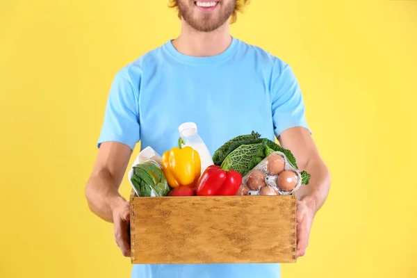 Leverans man håller trälåda med livsmedelsprodukter på färg bakgrunden, närbild — Stockfoto