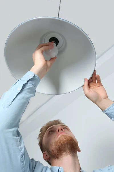 Man changing light bulb in pendant lamp indoors, low angle view — Stock Photo, Image