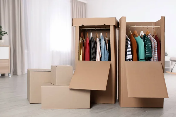 Cardboard wardrobe boxes with clothes on hangers indoors. Space for text