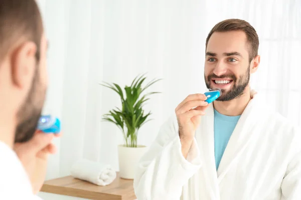 Young man using teeth whitening device at home — Stock Photo, Image