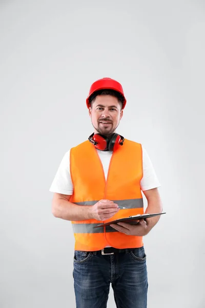 Ingeniero industrial masculino en uniforme con portapapeles sobre fondo claro. Equipo de seguridad —  Fotos de Stock