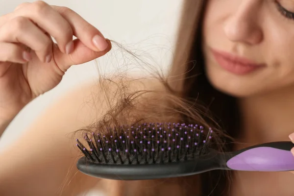 Woman untangling her hair from brush on light background, closeup — Stock Photo, Image