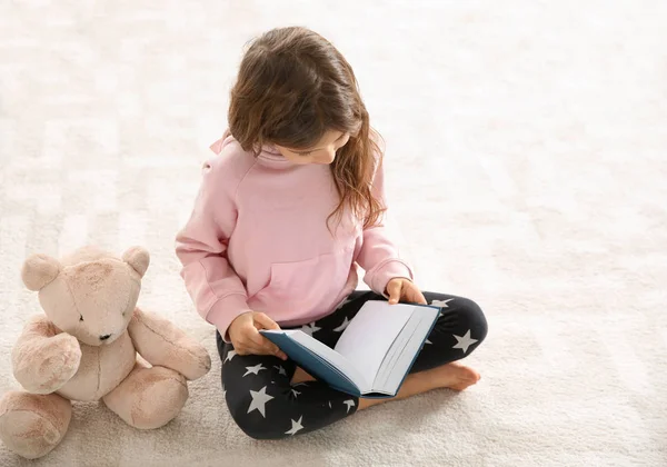 Χαριτωμένο μικρό κορίτσι με αρκουδάκι, διαβάζοντας το βιβλίο στο πάτωμα. Χώρο για το κείμενο — Φωτογραφία Αρχείου