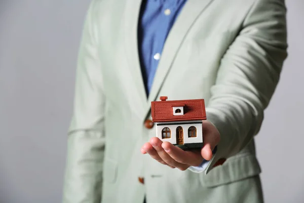 Agente masculino sosteniendo modelo de casa sobre fondo gris, primer plano. Seguro de hogar — Foto de Stock