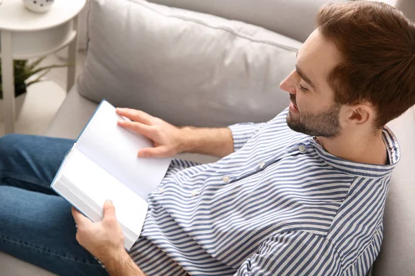 Schöner junger Mann liest Buch zu Hause auf dem Sofa — Stockfoto