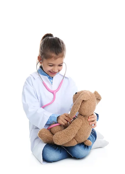 Симпатичный ребенок играет в доктора с мягкой игрушкой на белом фоне — стоковое фото