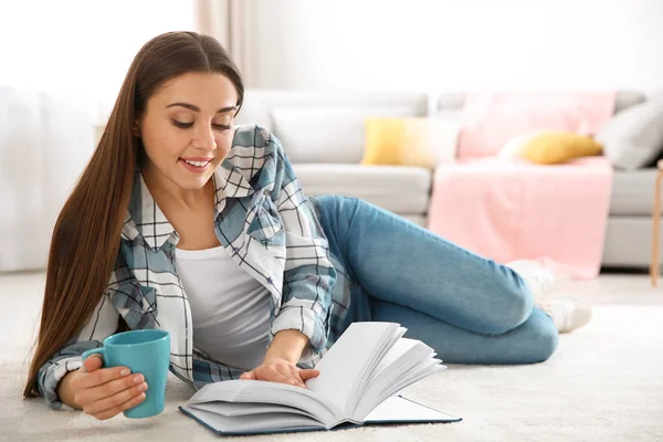 Piękna młoda kobieta z kubkiem kawy czytanie książki na piętrze w domu. Miejsca na tekst — Zdjęcie stockowe