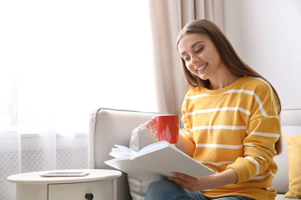 Evde kanepede kitap okumak kahve fincan genç kadınla — Stok fotoğraf