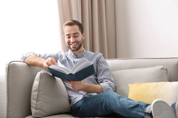 Schöner junger Mann liest Buch zu Hause auf dem Sofa — Stockfoto