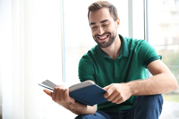 Junger Mann liest Buch am Fenster zu Hause — Stockfoto