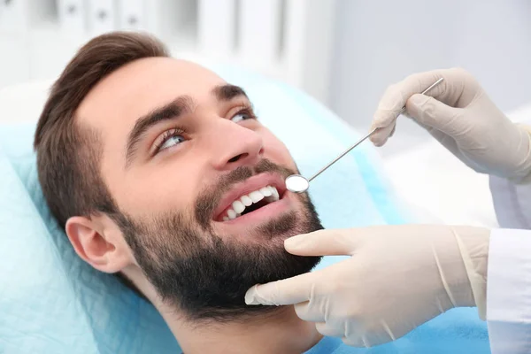 Zahnarzt untersucht Zähne des jungen Mannes mit Spiegel im Krankenhaus — Stockfoto