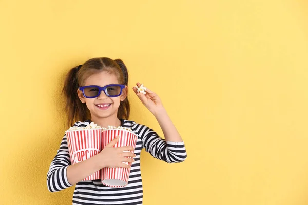 Niedliches kleines Mädchen mit Popcorn und Gläsern auf farbigem Hintergrund. Raum für Text — Stockfoto