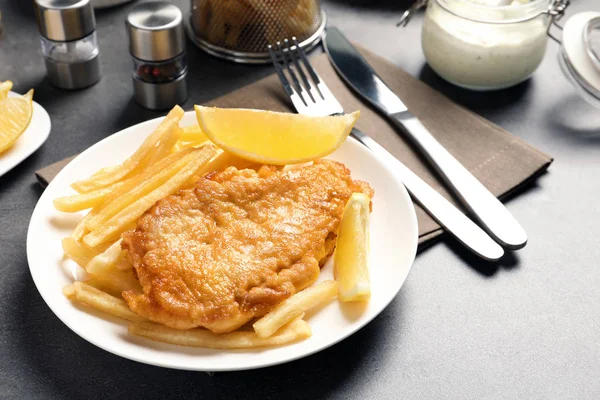 Plate with British traditional fish and potato chips on grey table