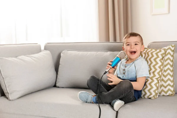 Mignon garçon drôle avec microphone assis sur le canapé à la maison. Espace pour le texte — Photo
