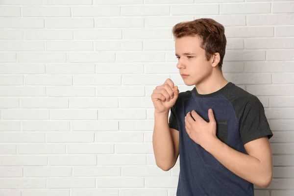 Tonårspojke lider av hosta nära tegelvägg. Utrymme för text — Stockfoto