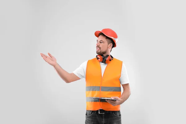 Wirtschaftsingenieur in Uniform mit Klemmbrett auf hellem Hintergrund. Sicherheitsausrüstung — Stockfoto