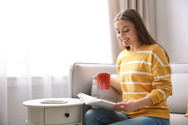 Fiatal nő csésze kávé olvasókönyv otthon a kanapén — Stock Fotó