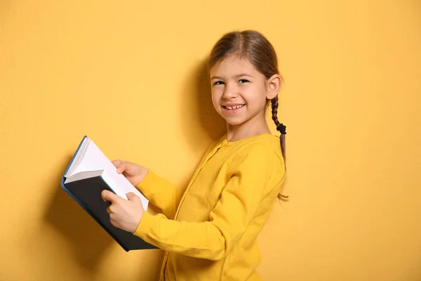 Söt liten flicka med bok på färg bakgrund — Stockfoto