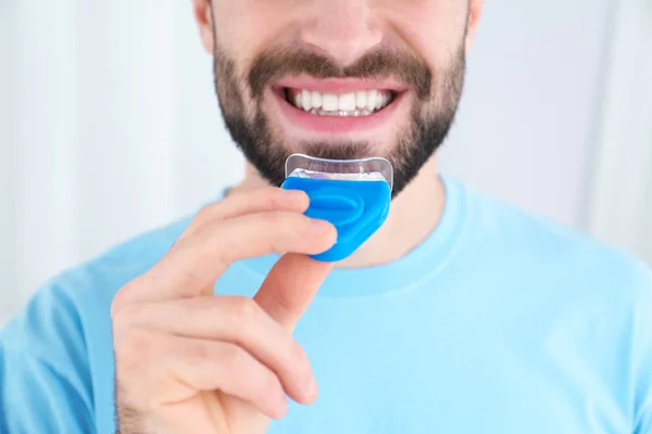 Gebruik teeth whitening apparaat op lichte achtergrond, close-up jongeman — Stockfoto