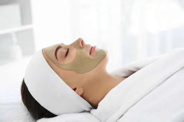 Mooie vrouw met klei masker op haar gezicht in spa salon — Stockfoto