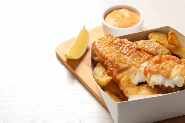 Einwegbehälter mit traditionellem britischem Fisch und Kartoffelchips auf Holzgrund — Stockfoto