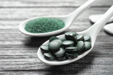 Spirulina hapları ve toz üzerinde ahşap masa, tatlı kaşığı